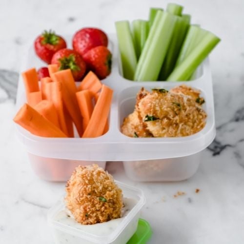 a lunch container filled with baked nuggets, carrot sticks, celery sticks, and strawberries