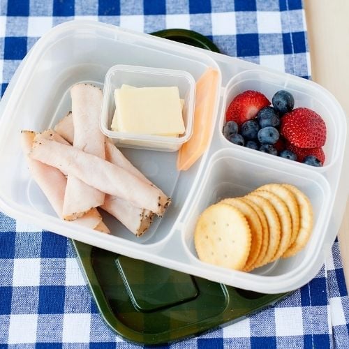 a lunch container filled with rolled deli turkey, crackers, silced cheese, and berries