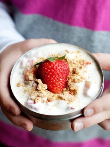 kid holding a small thermos container filled with a strawberry parfait