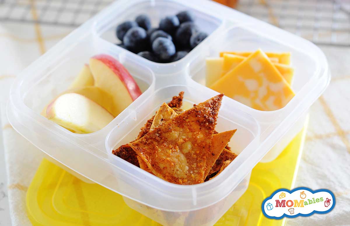 homemade doritos in a lunchbox with apple slices, blueberries and cheese slices on the other containers