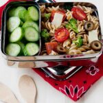 pizza pasta salad in a metal lunch box with cucumber slices on the side