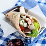 close up of a greek chicken pita wrap made with chicken, lettuce, tomatoes, feta, and hummus