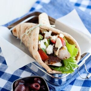 close up of a greek chicken pita wrap made with chicken, lettuce, tomatoes, feta, and hummus