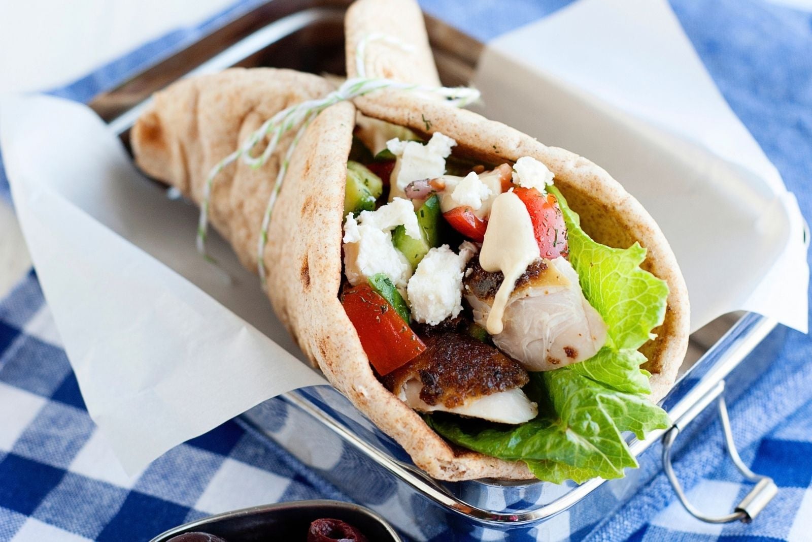 close up of a greek chicken pita wrap made with chicken, lettuce, tomatoes, feta, and hummus