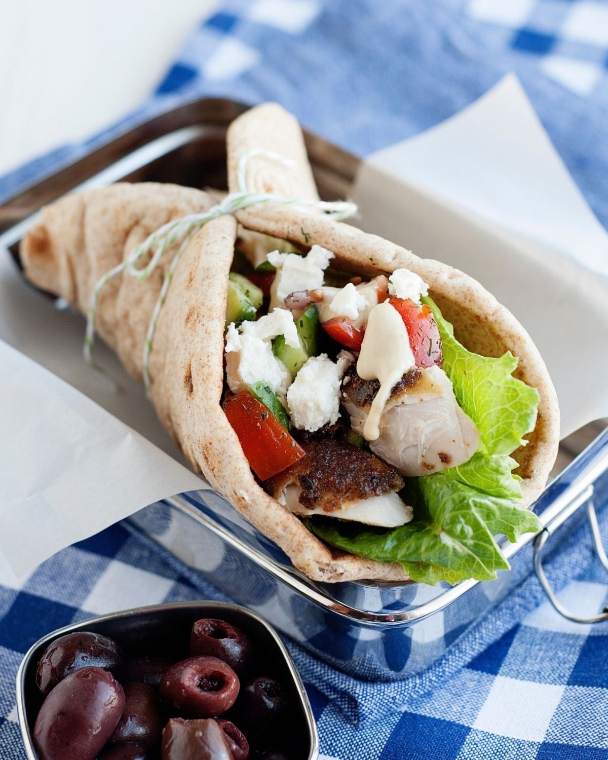 close up of a greek chicken pita wrap made with chicken, lettuce, tomatoes, feta, and hummus