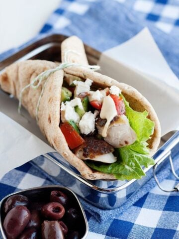close up of a greek chicken pita wrap made with chicken, lettuce, tomatoes, feta, and hummus