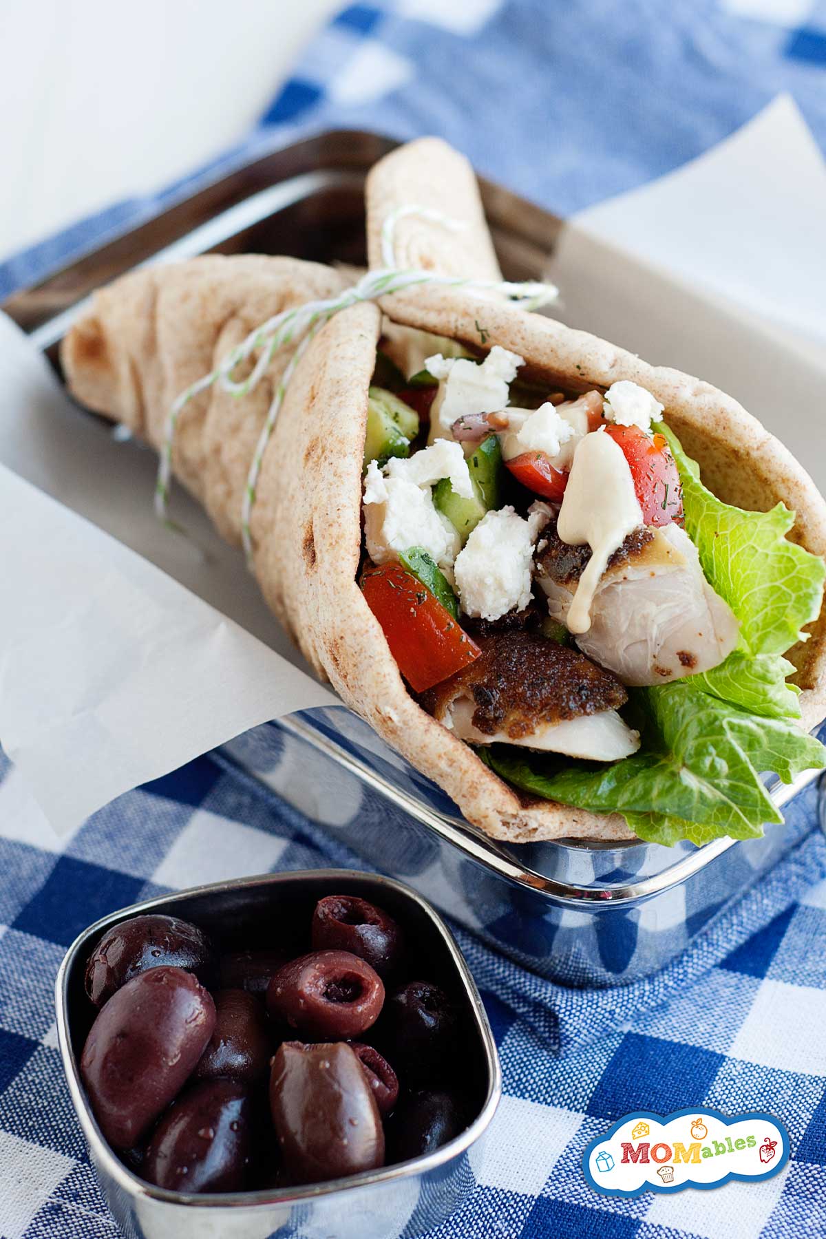 greek chicken pita wrap in a lunchbox and some olives on the side.