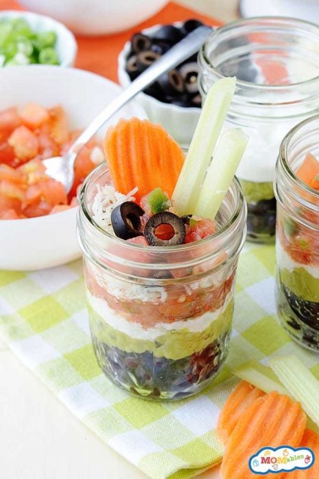 black beans, guacamole, salsa, tomatoes, cheese, and black olives layered into a glass jar and served with fresh vegetables