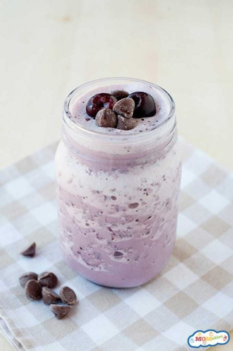a purple smoothie in a glass topped with frozen cherries and chocolate chips.