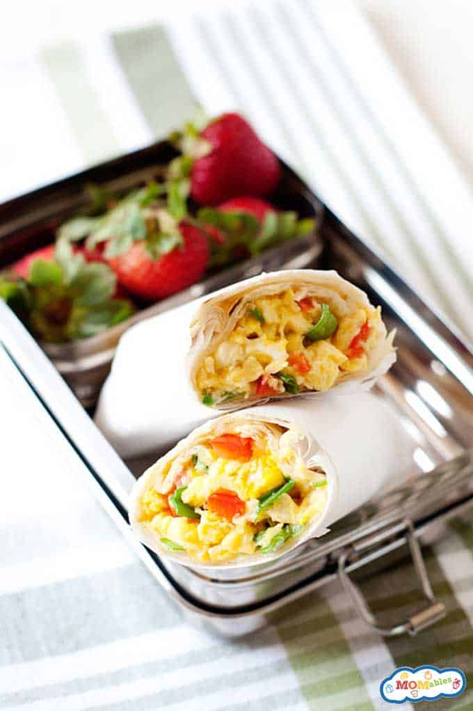 Breakfast burritos wrapped in parchment in a lunchbox with fresh berries.