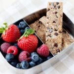 Healthy Chocolate Chip Snack Bars in a tin lunchbox with strawberries, blueberries and raspberries on the side