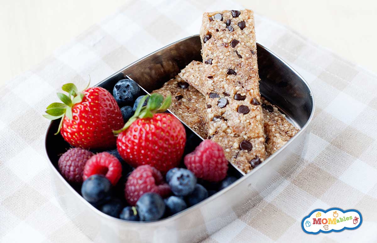 Healthy Chocolate Chip Snack Bars in a tin lunchbox with strawberries, blueberries and raspberries on the side