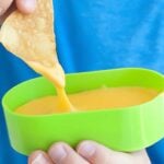 a chip being dipped into cheese sauce