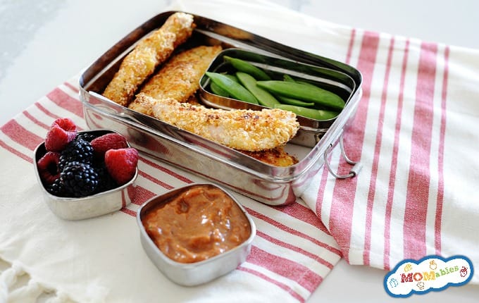 image: small lunchbox with four baked chicken tenders, and snow peas. Smaller containers hold dip and fresh berries. 