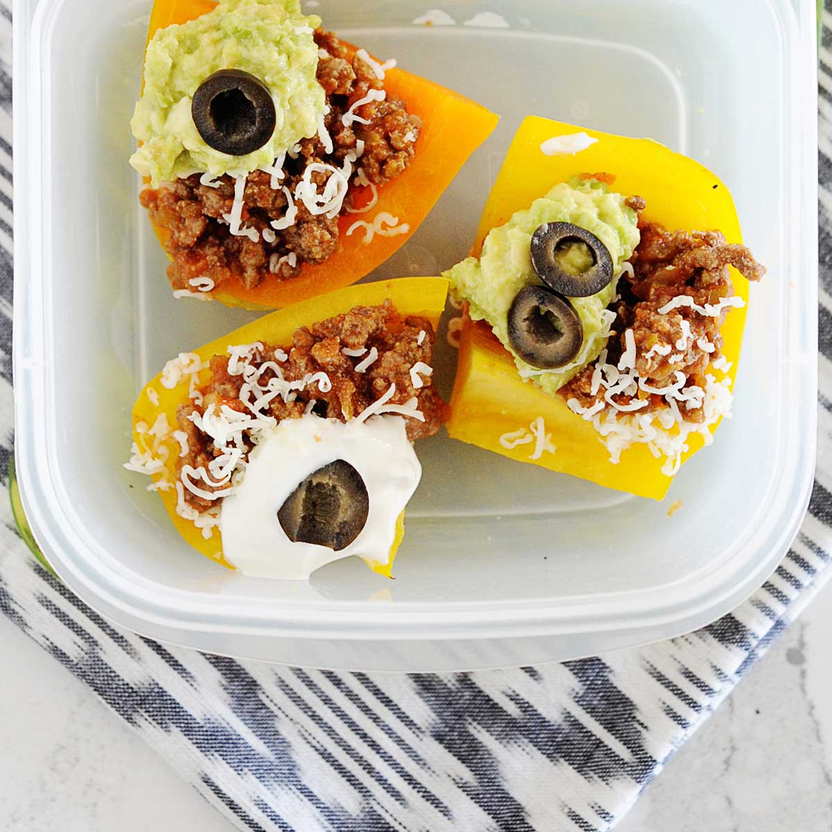 a lunch container filled with bell pepper nachos and topped with cheese, sour cream, guacamole, and black olives. 