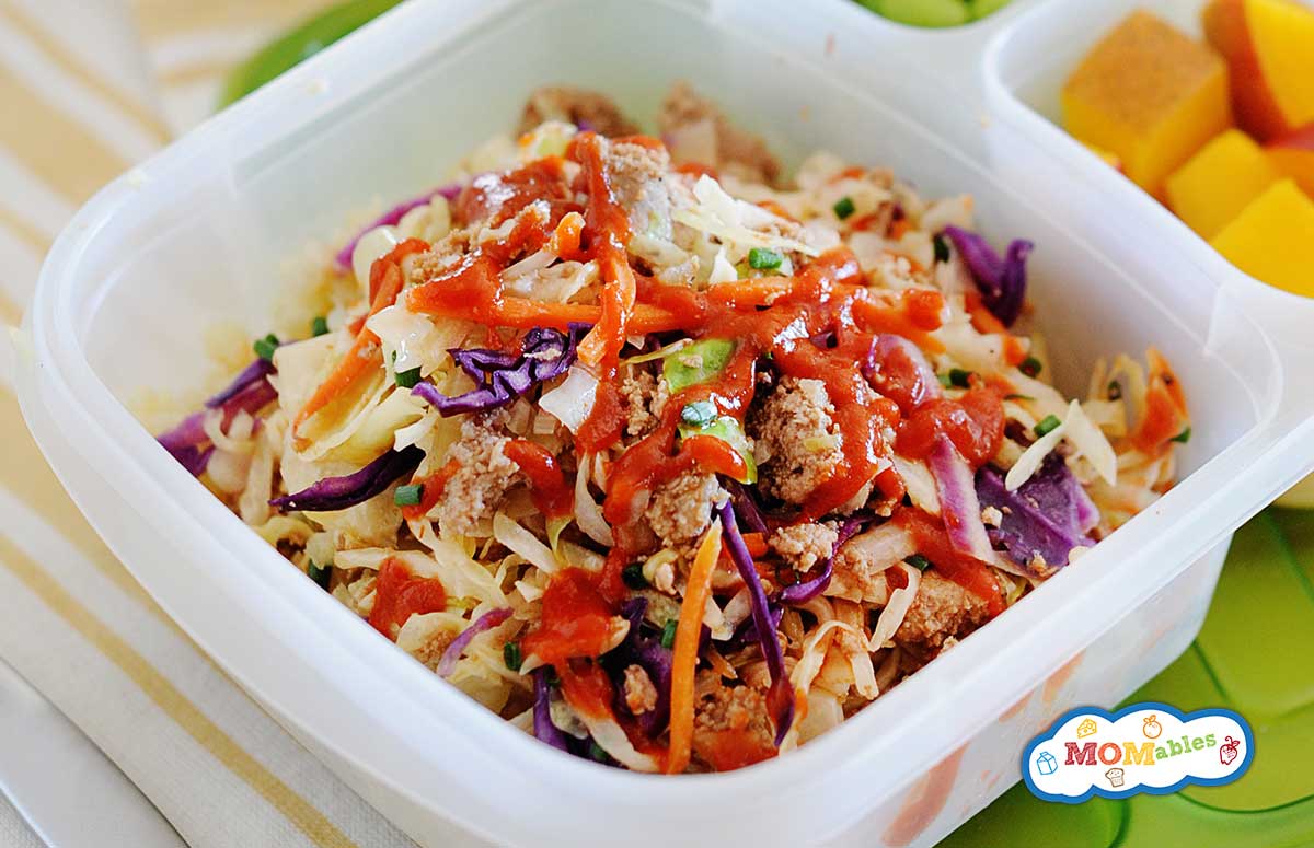 eggroll in a bowl served in a lunch container with cubed mango and steamed edamame.