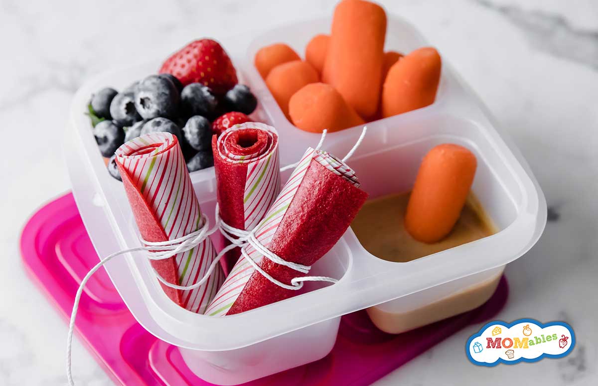 fruit leather in a plastic lunch container with berries and carrots on the side