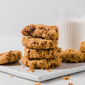 4 oatmeal cookies stacked on top of each other next to a glass of milk.