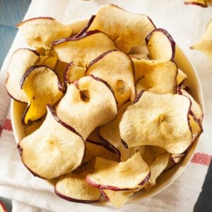 small bowl of curly apple chips, next to a few fresh apples