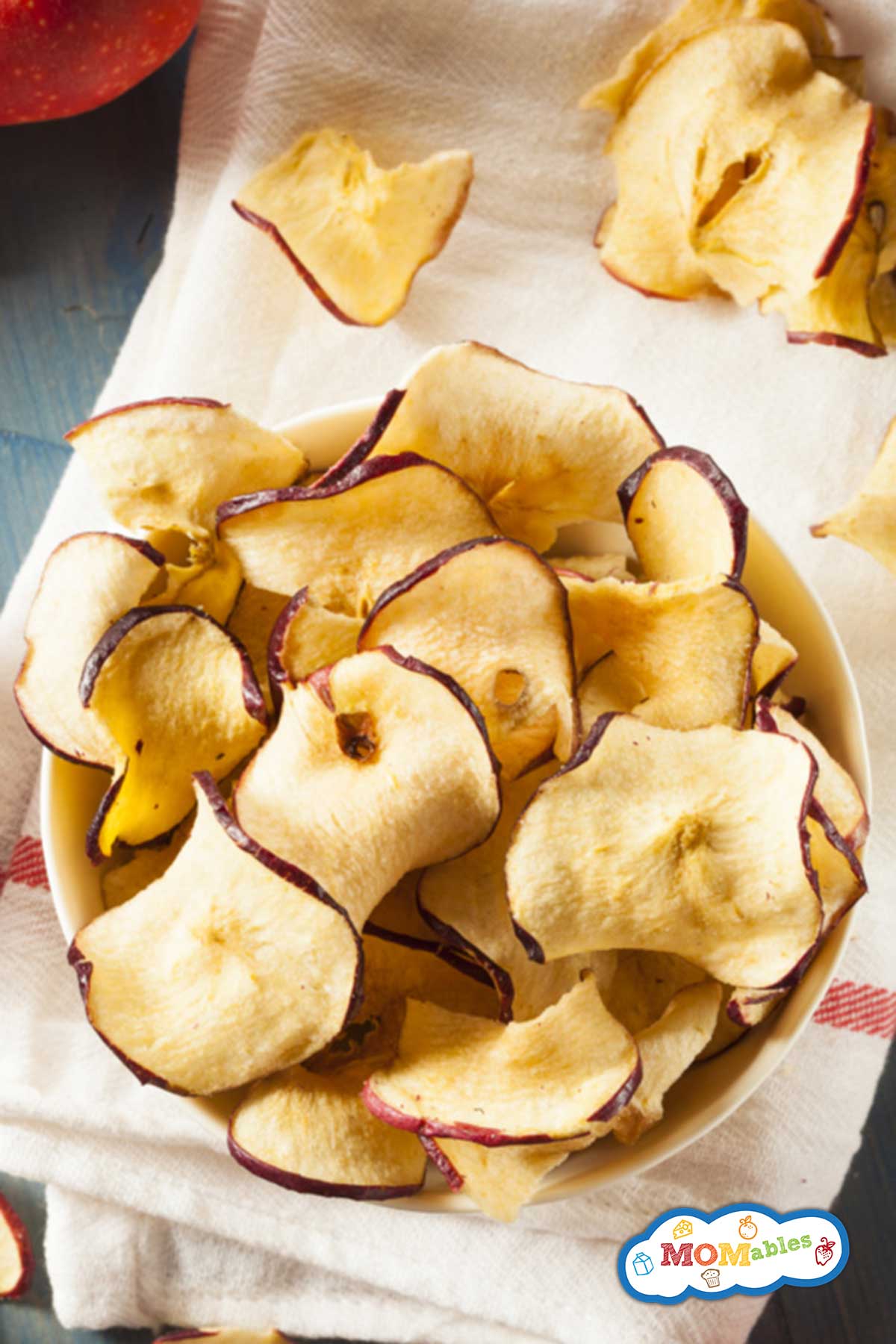 small bowl of curly apple chips, next to a few fresh apples