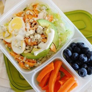 Buffalo Chicken Salad with dressing in a divided lunch container. Carrot sticks and blueberries fill the other two container sides
