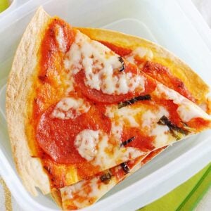tortilla pizza in a lunch box with tomatoes, baby carrots and apple slices