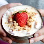hands holding a small thermos container filled with a strawberry parfait