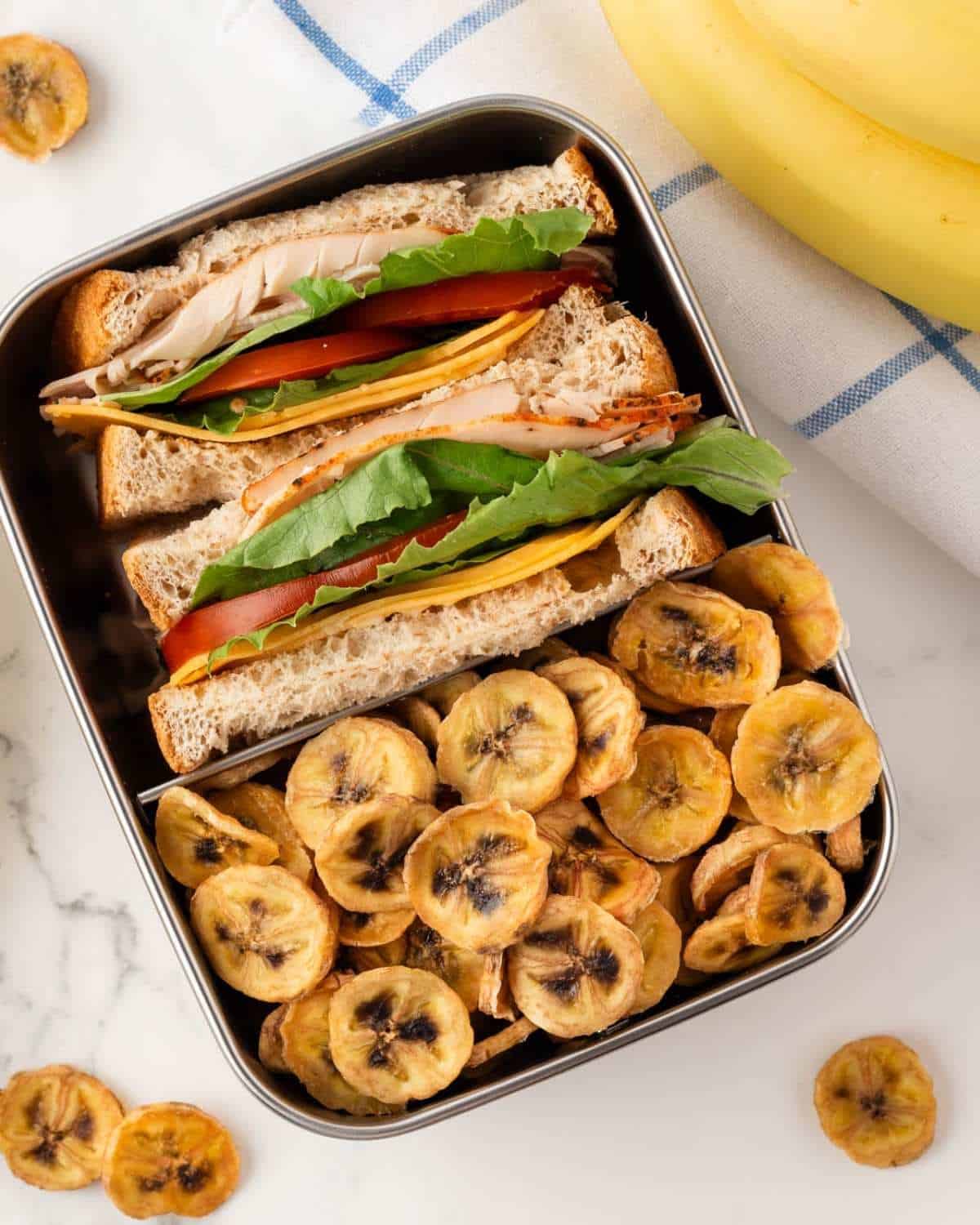baked banana chips in a snack box with a sandwich on the side