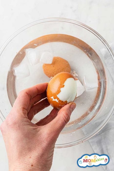 a hard boiled egg partially peeled being held over a bowl of ice water