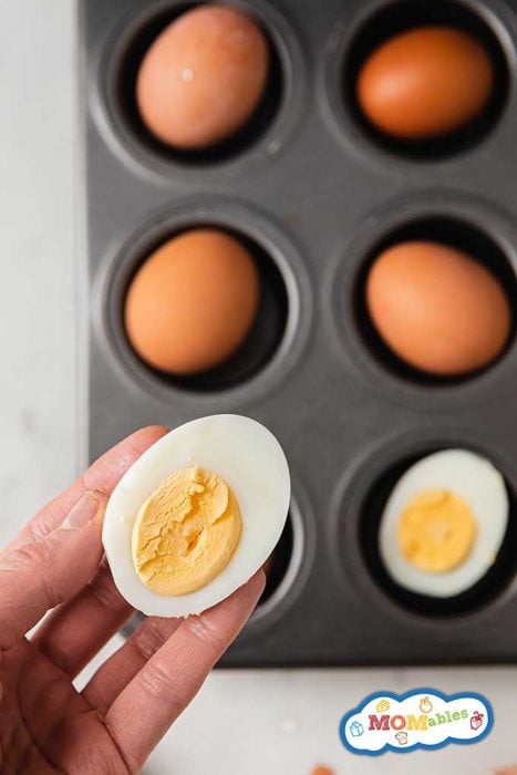 holding half a hard boiled egg up over a muffin tin of boiled eggs 