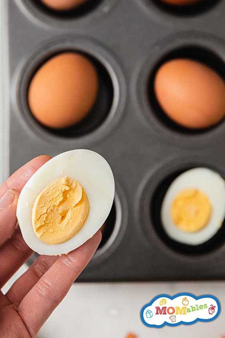 hand holding half a boiled egg over a muffin tin of baked eggs