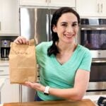 a woman holding up a paperback lunch in a kitchen