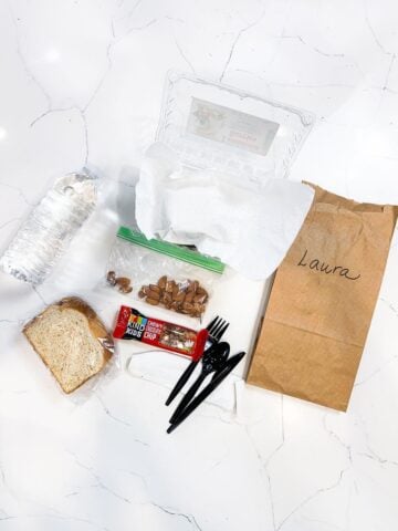 a sandwich, a bottle of water, a small bag of almonds, a granola bar, and a brown paper bag with utensils
