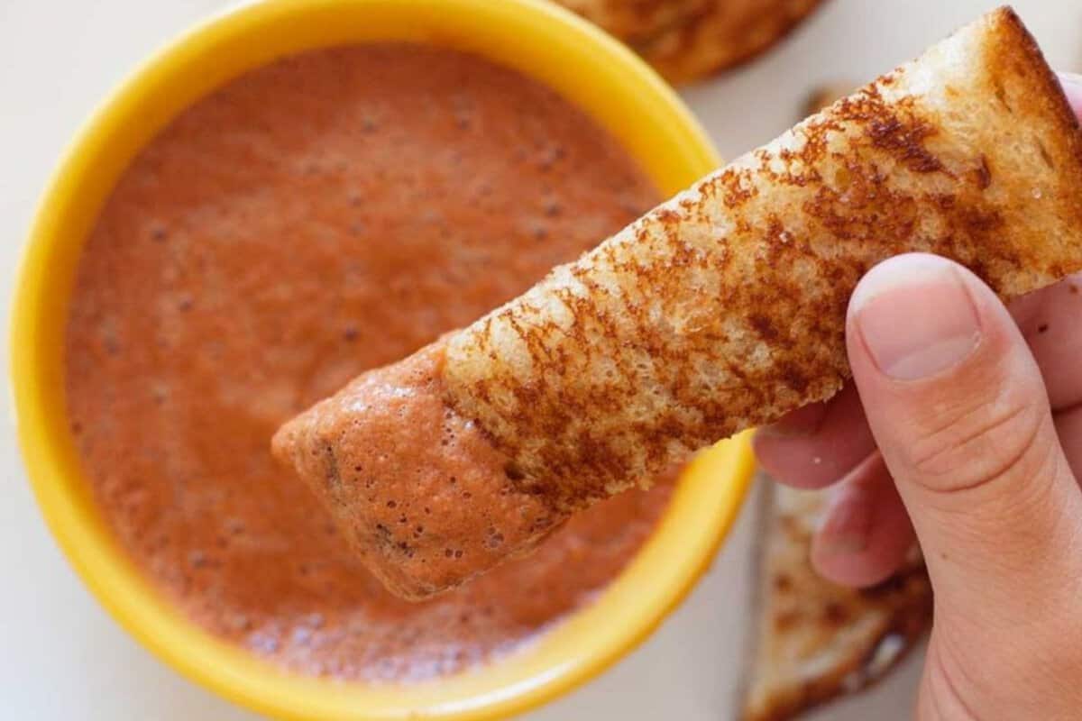 a kid dipping a grilled cheese dipper in tomato soup