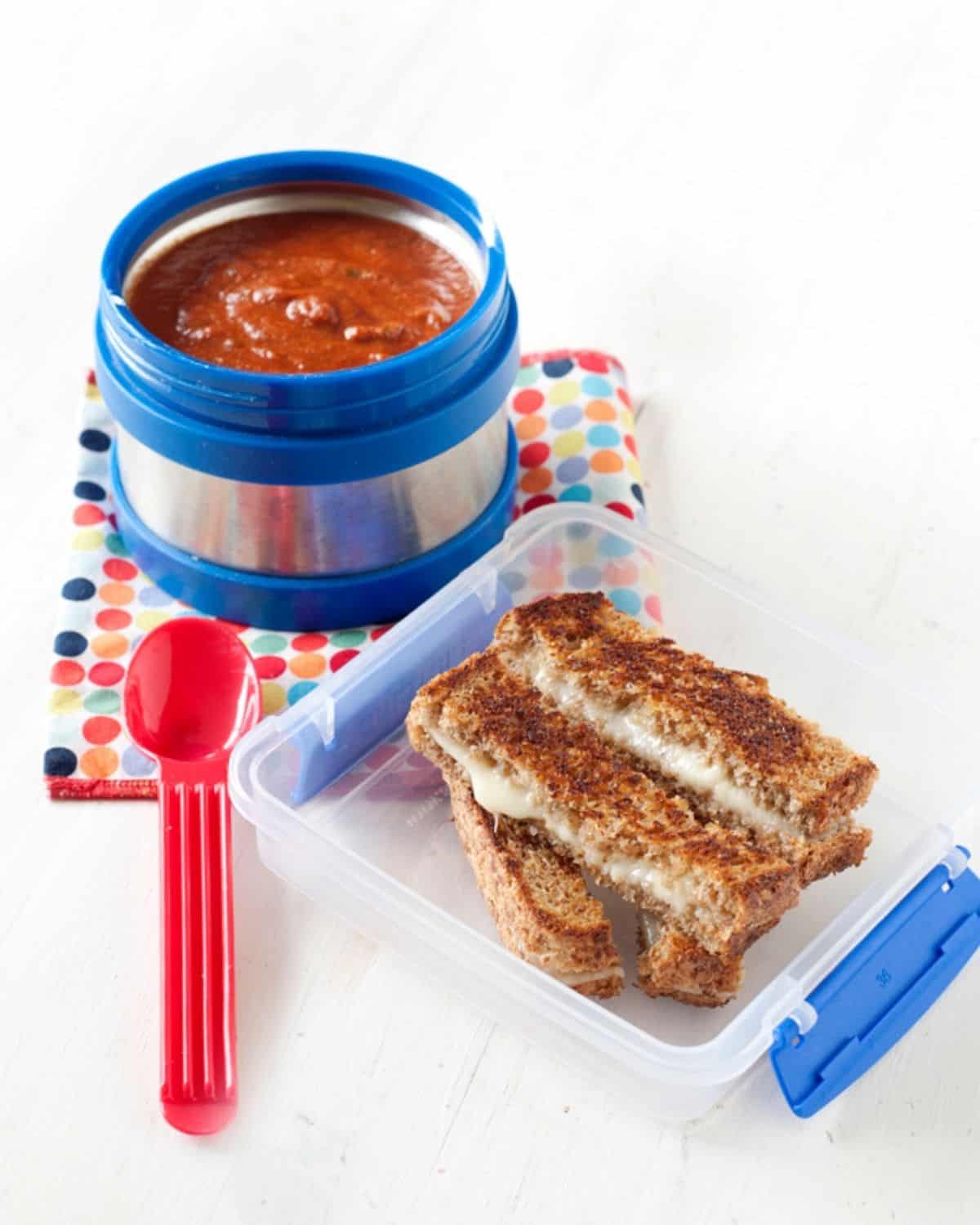 a lunchbox with cheese dippers and a thermos with tomato soup