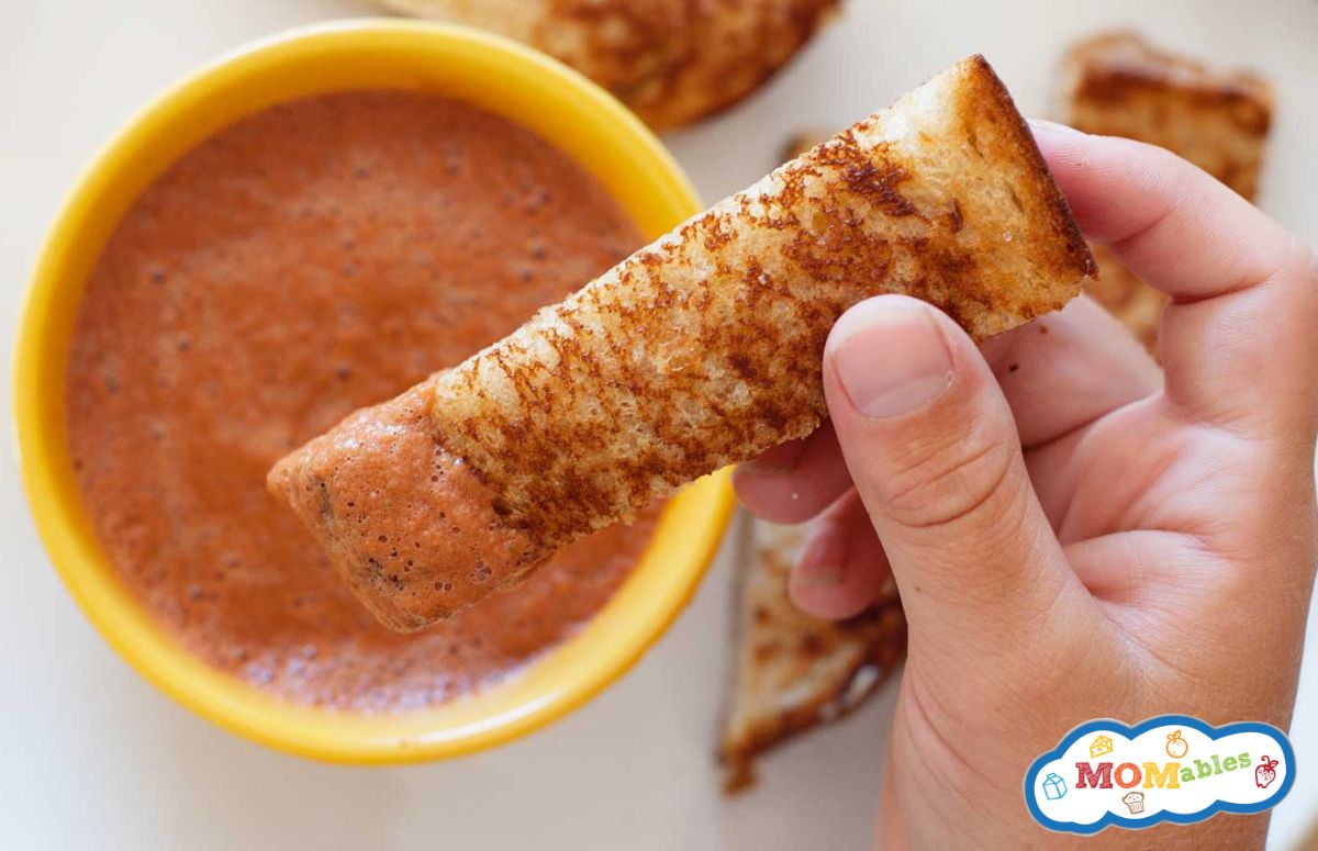 a kid dipping a grilled cheese dipper in tomato soup