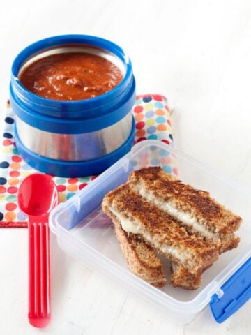 a lunchbox with cheese dippers and a thermos with tomato soup