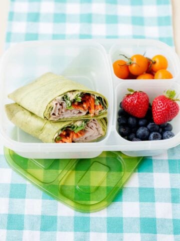 Hummus wraps in a lunch box with fruit on the side