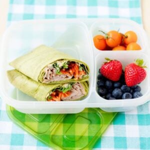 turkey hummus wrap halved in a lunch box with fruit on the side