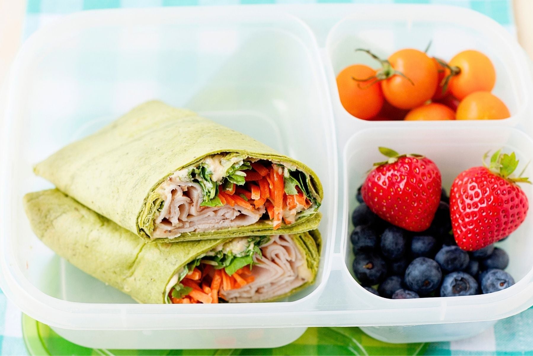 turkey hummus wrap halved in a lunch box with fruit on the side