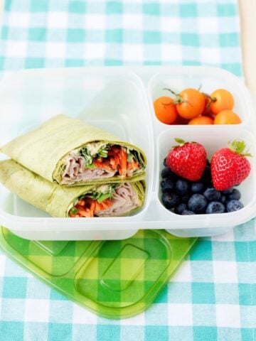 turkey hummus wrap halved in a lunch box with fruit on the side