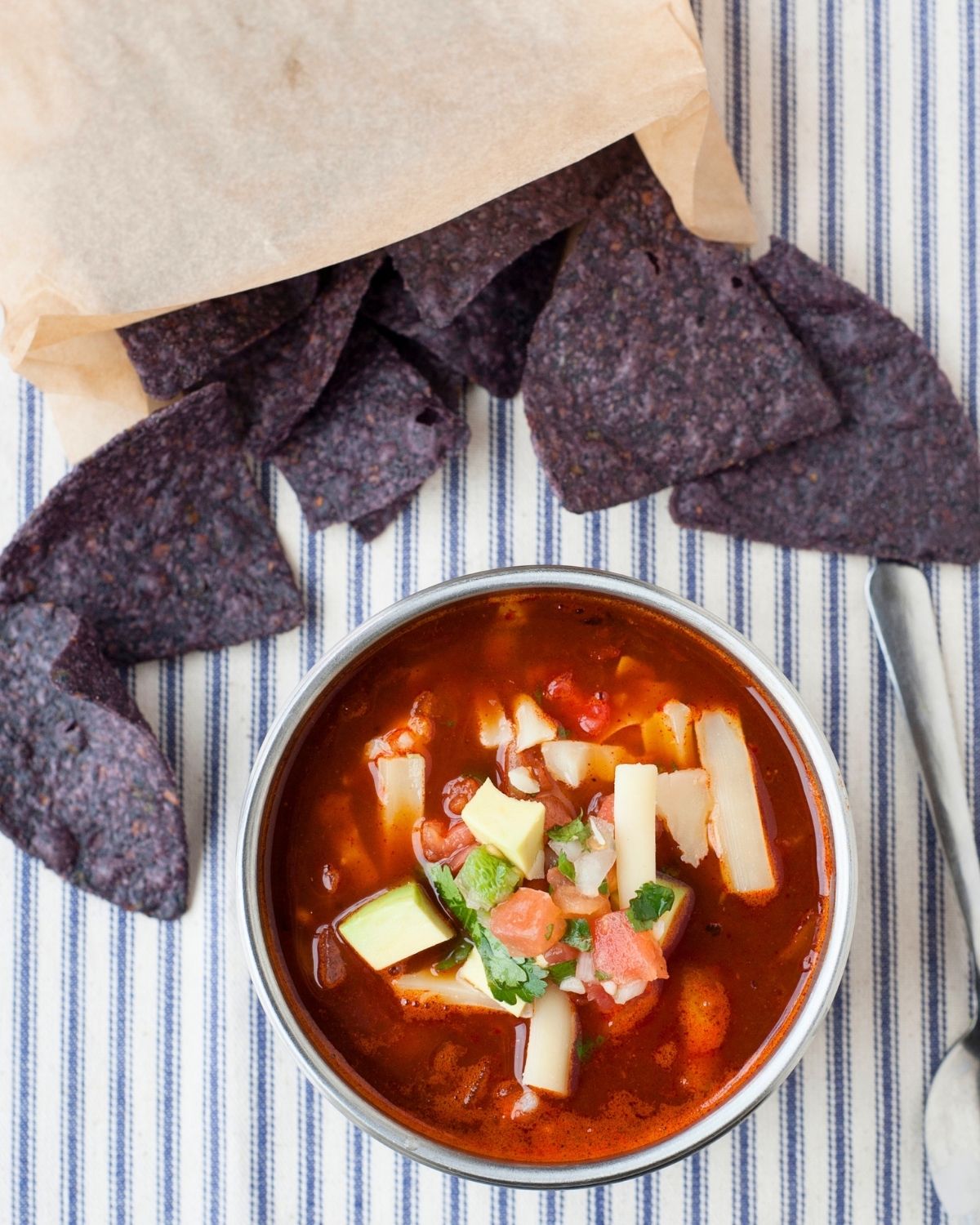 thermos of enchilada soup with shredded cheese on top and blue corn chips spilled behind the thermos