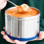 hands holding a thermos with tomato tortellini soup