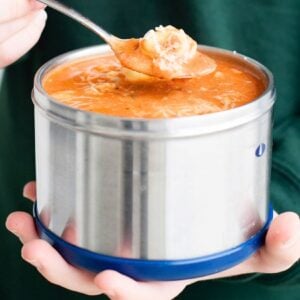 hands holding a thermos with tomato tortellini soup