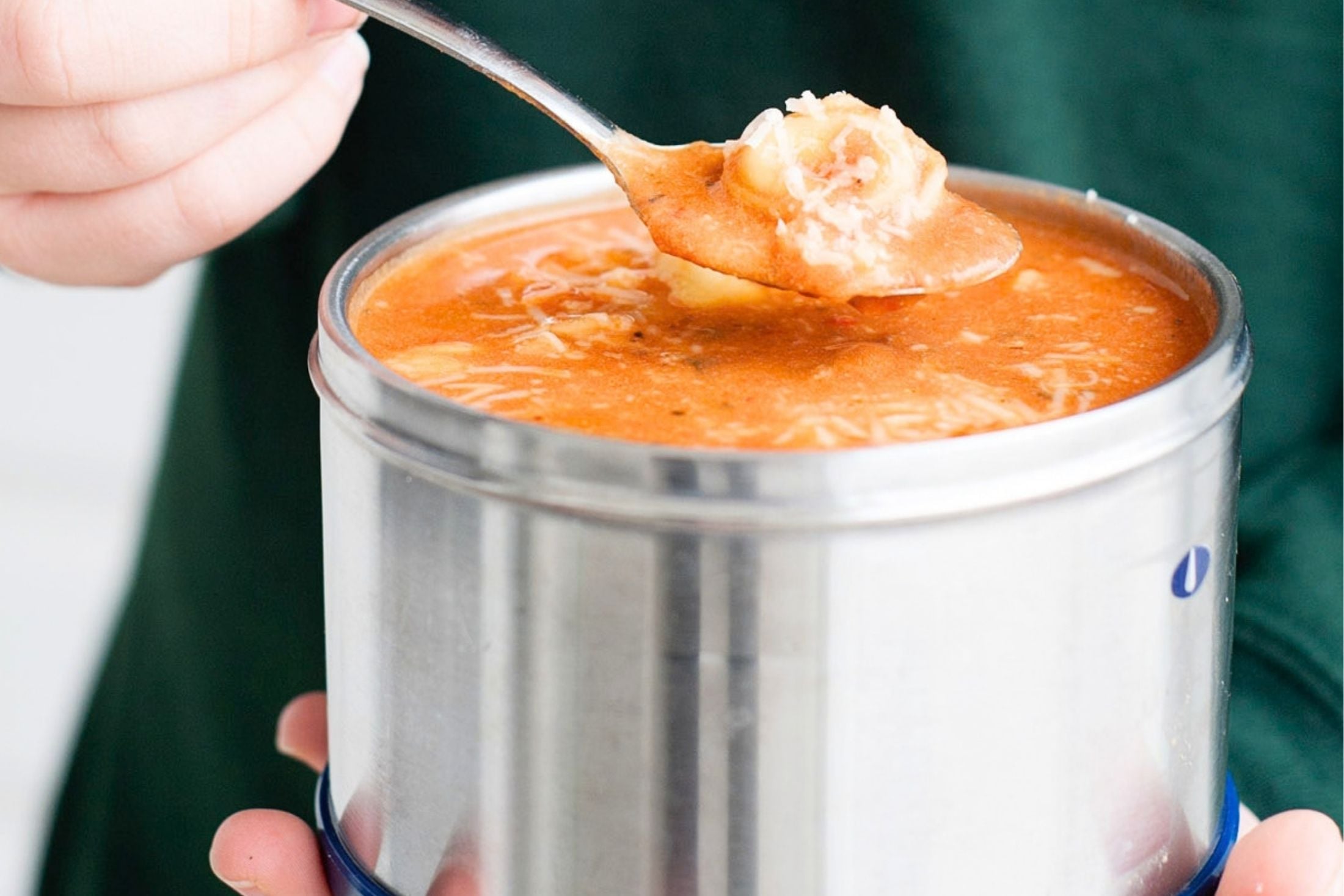 hands holding a thermos with tomato tortellini soup