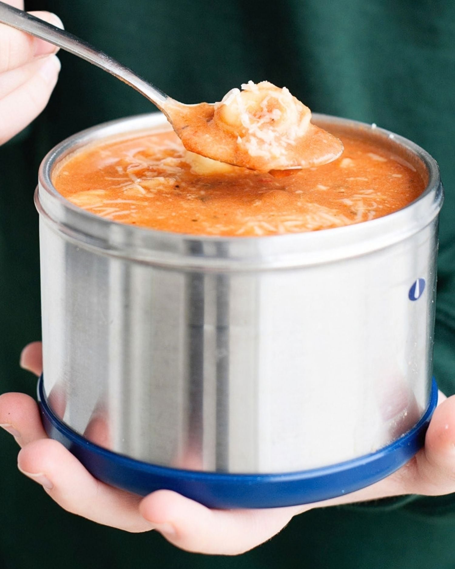 hands holding a thermos with tomato tortellini soup