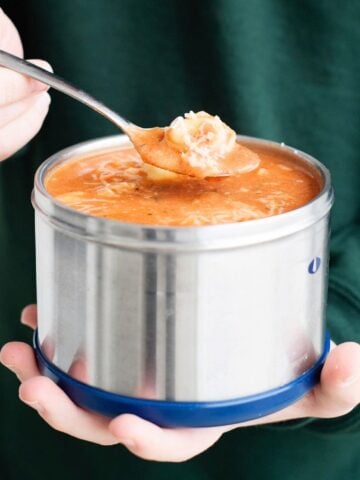 hands holding a thermos with tomato tortellini soup