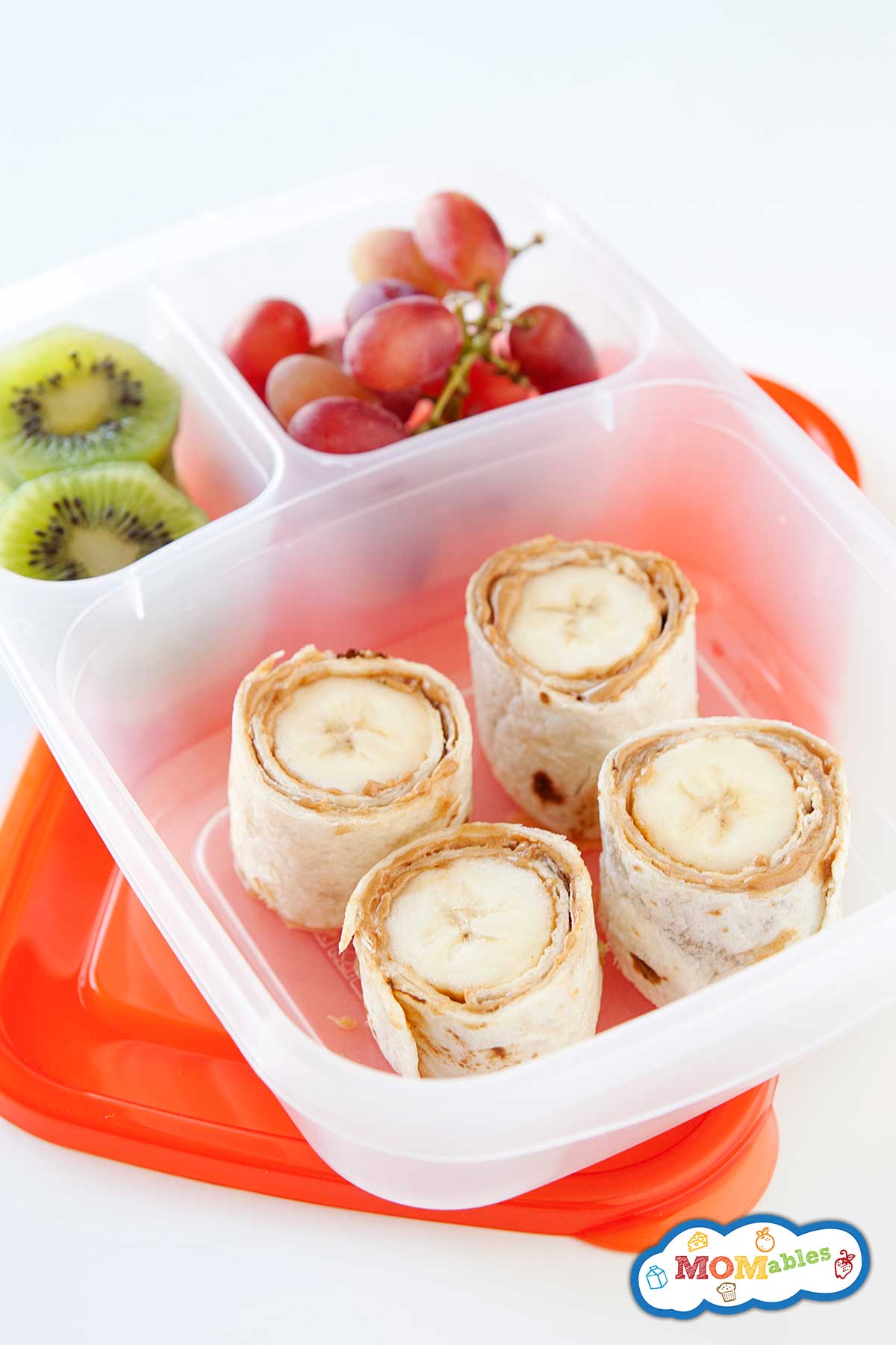 Peanut butter and banana sushi packed into a lunch container with grapes and kiwi.
