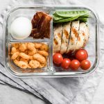 sliced chicken breast, vegetables bacon slices and a boiled egg in a lunch container