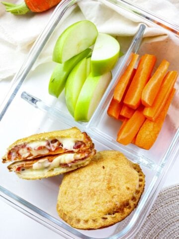 pizza uncrustable packed into a lunch container with sliced apples and carrots